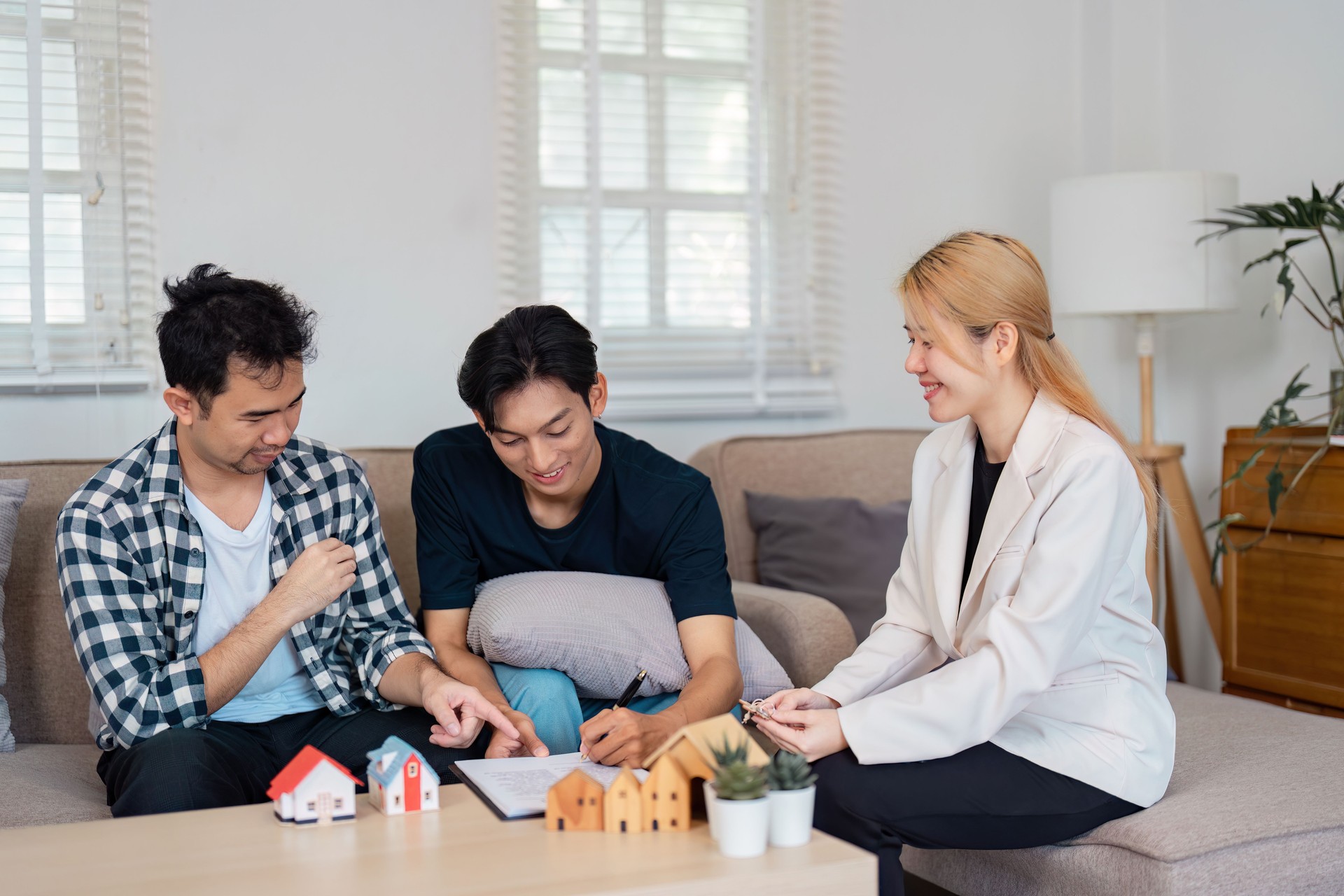 LGBTQ couple discussing home purchase details with a real estate agent in a modern living room, showcasing collaboration.